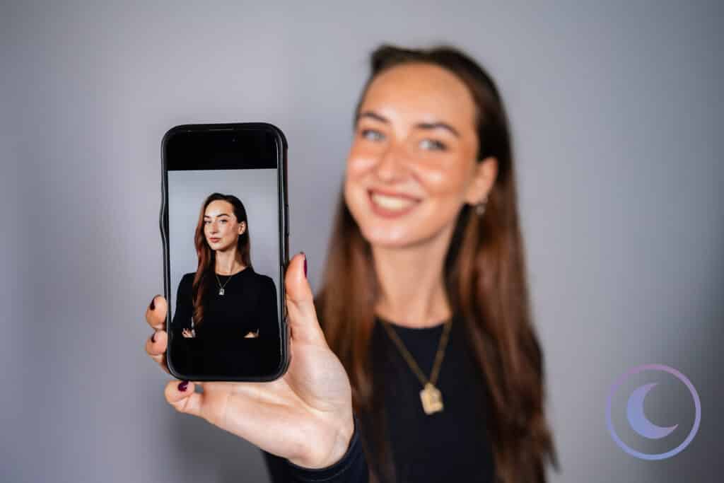 Woman smiling while showing her professional portrait on a smartphone taken with Luna Events Headshot Booth
