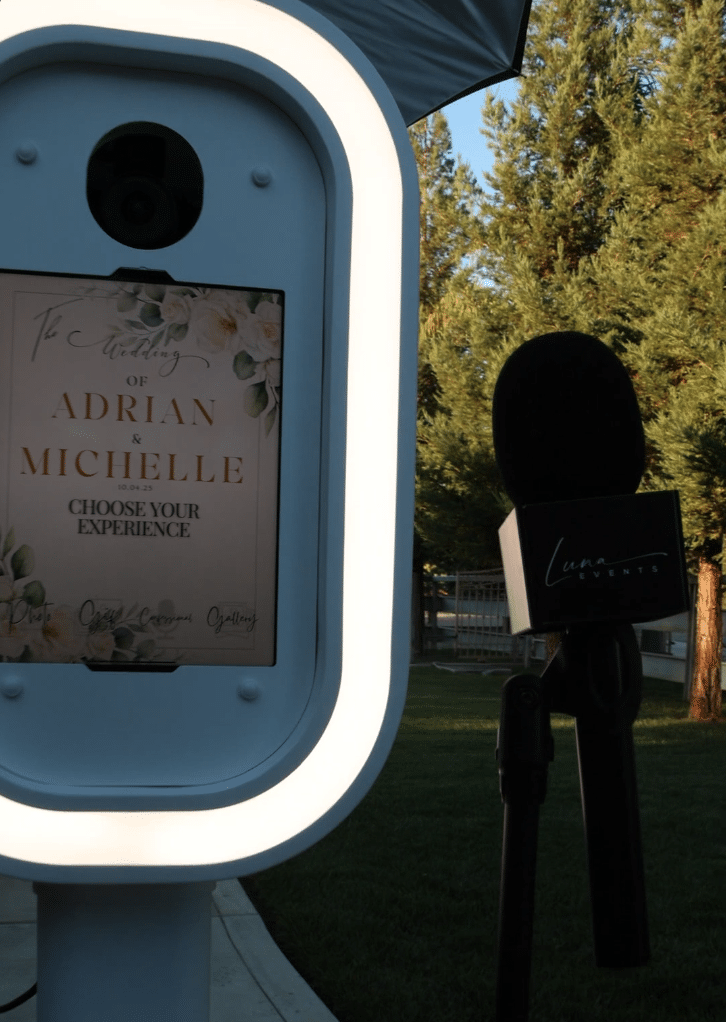 Video Confessional Booth setup at a wedding, featuring a lighted photo booth screen and a Luna Events microphone on a stand outdoors.