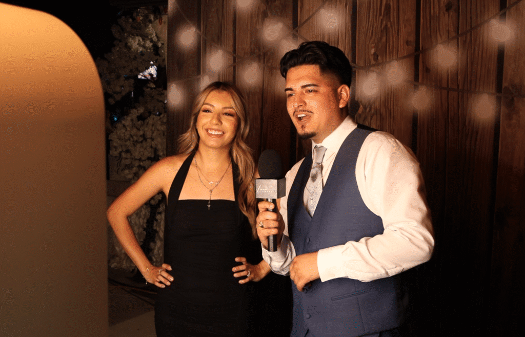 Couple recording a fun video confessional at Luna Events’ booth with warm studio lighting and wooden backdrop